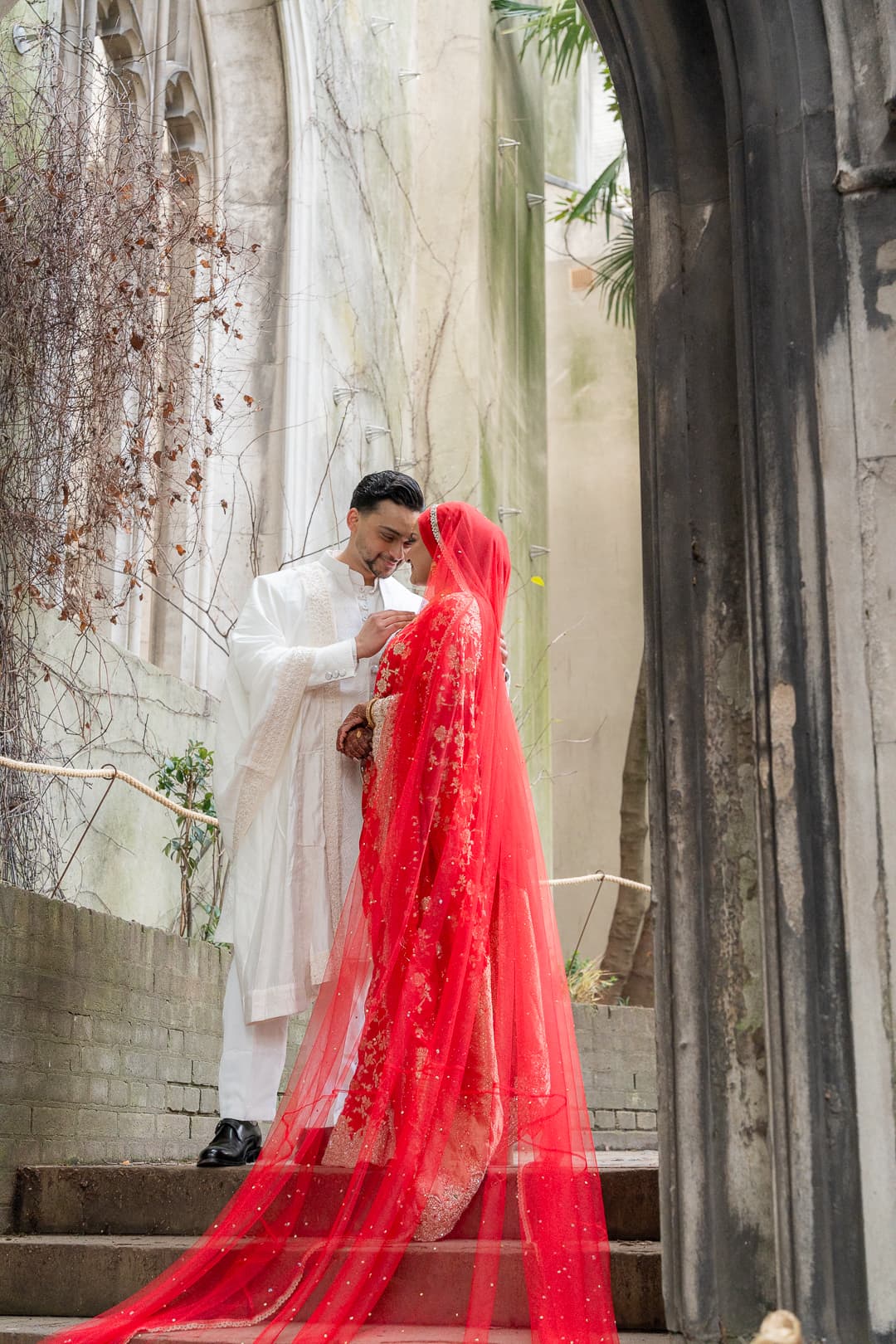 Couple standing beneath stone arches during a warmly lit wedding portrait.