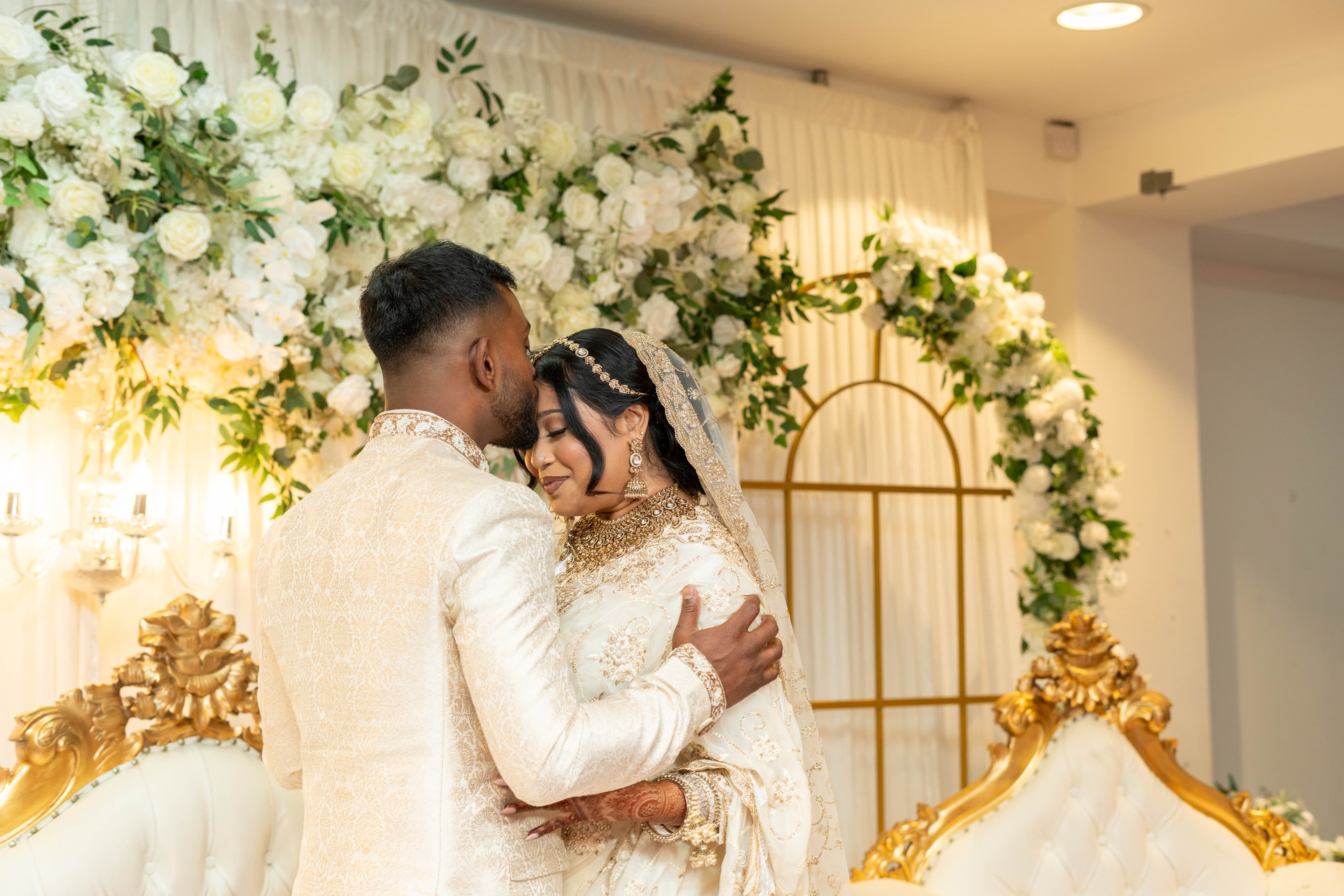 Couple embracing in front of white floral wedding decor.